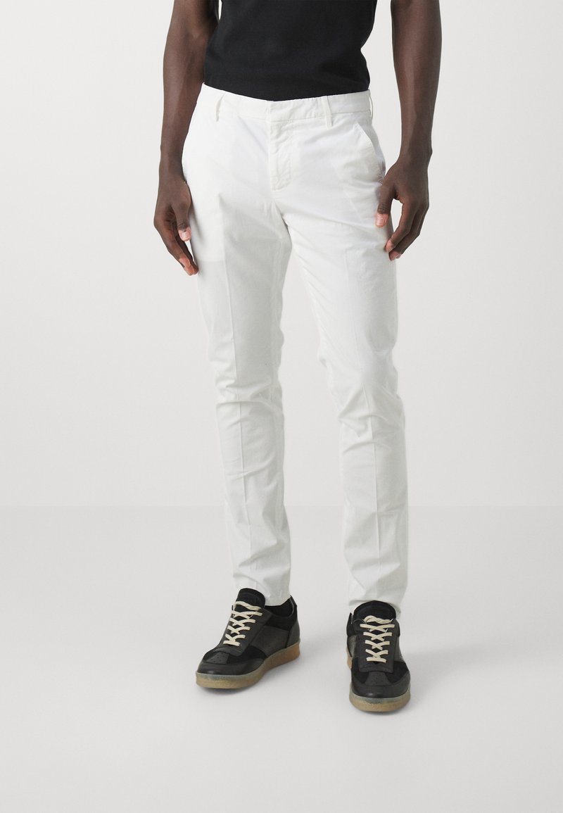 Pantaloni bianchi in cotone con vestibilità slim, caratterizzati da un design con tasche anteriori. Abbinati a sneaker nere con parte superiore texturizzata e lacci beige.