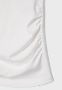 Krupni plan bijele tkanine s naboranim detaljem duž desnog bočnog šava, prikazuje glatku teksturu i uredan rub.