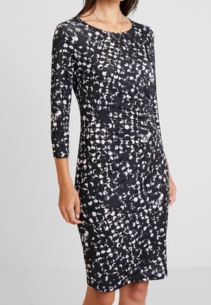 Robe noire avec des manches trois-quarts, présentant un motif blanc et gris dispersé, le tissu a une texture douce et extensible avec un détail de taille froncée.