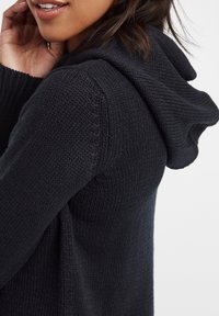 Donkergrijze gebreide hoodie met gestructureerde stof, losse pasvorm en een zachte, opgevouwen capuchon. Beschikt over ribgebreide manchetten en zoom.