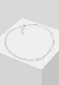 Collier délicat en chaîne d'argent avec de petites mailles et un fermoir mousqueton, présenté sur une surface blanche inclinée.
