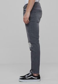Grå slim-fit jeans med slitte kne detaljer og en klassisk fem-lomme design, kombinert med svarte lave sneakers.