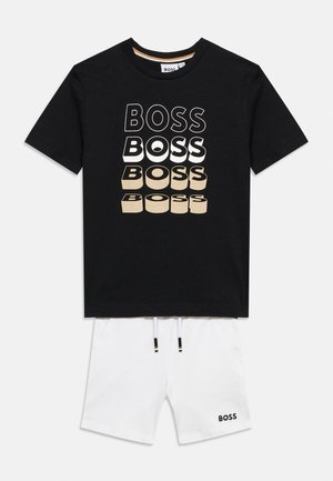 Crna majica kratkih rukava s natpisom "BOSS" u četiri stilizirana reda, uparena s bijelim šorcevima na vezanje s malim logom "BOSS".
