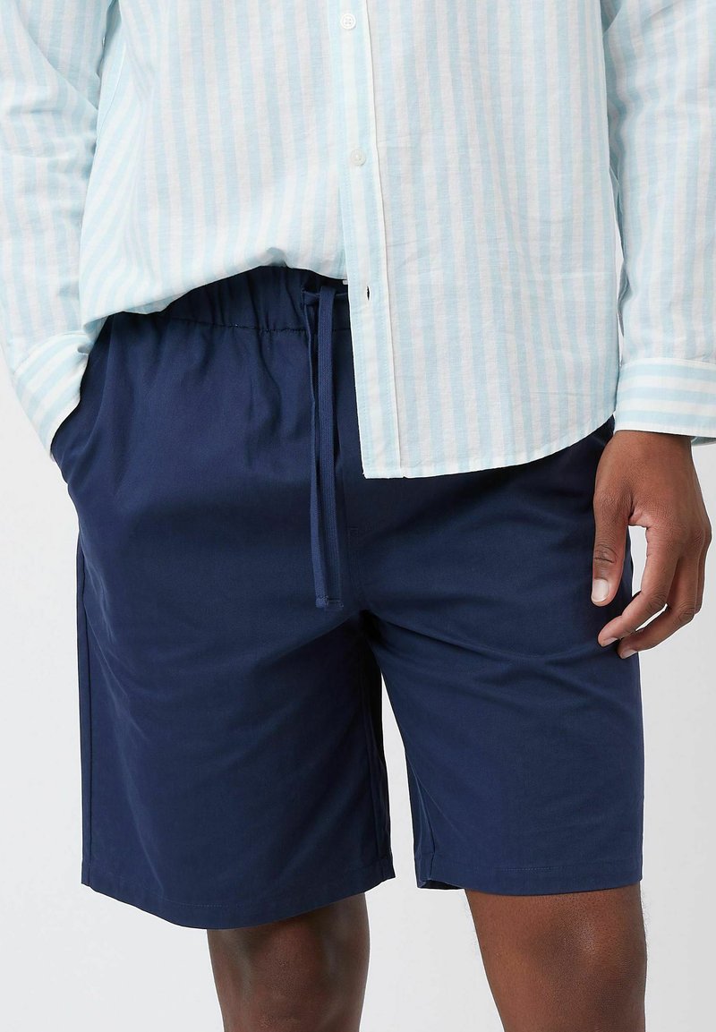 Shorts azul marino hechos de tela ligera con cinturilla elástica y cordón. Combinados con una camisa de botones a rayas azul clara.