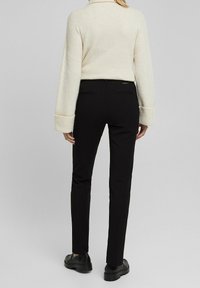 Svarta, slim-fit byxor med en slät textur, med bakfickor och midjeband, i kombination med en krämfärgad, ribbad stickad tröja.