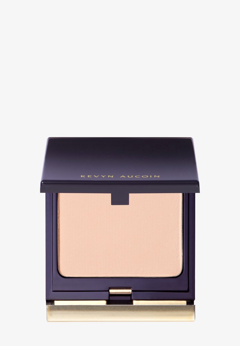 Compact powder in a navy blue case with gold lettering, featuring a smooth beige powder inside and a hinge opening mechanism.