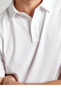 Biała koszulka polo wykonana z miękkiej bawełny, z kołnierzykiem zapinanym na dwa guziki, krótkimi rękawami oraz dyskretnym haftowanym logiem na klatce piersiowej.