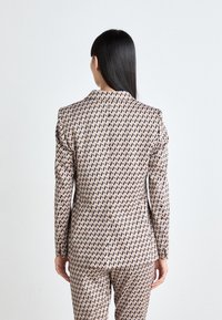 Maßgeschneiderte Blazer und passende Hose aus gemustertem Stoff mit einem Diamantdesign in pastellfarbenen Tönen, glänzender Textur und strukturierten Schultern.