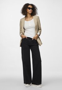 Beige sáčko přes bílé žebrované tílko, doplněné černými kalhotami s širokými nohavicemi a černými teniskami s bílou podešví. Na očích černé sluneční brýle.