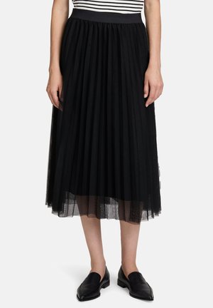 Gonna plissettata in tulle nera con un ampio elastico in vita, caratterizzata da un design trasparente a strati e una fodera solida. Indossata con scarpe nere senza lacci.