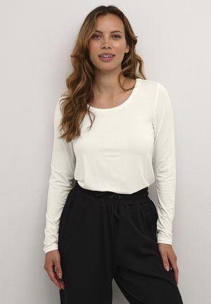 Long-sleeve, cream-colored top with a rounded neckline, paired with black drawstring pants, featuring a relaxed fit and soft texture.