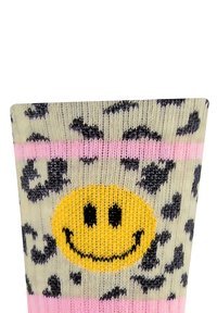 Kniestrümpfe mit beigem Grund, schwarzen Leopardenflecken, pinken Streifen und einem zentralen gelben Smiley-Design. Hergestellt aus weichem, strukturiertem Stoff.