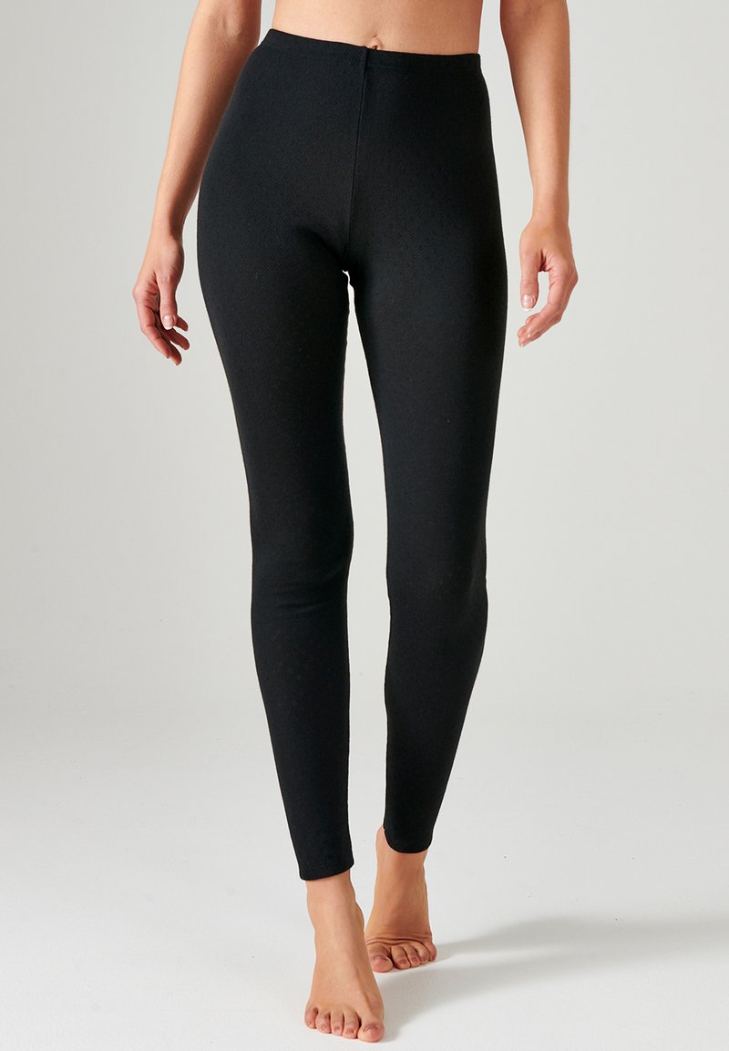 Leggings negros de tejido texturizado, con un diseño ajustado y cintura alta. La superficie tiene un patrón sutil y sin costuras visibles.