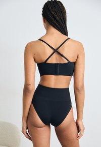 Black high-waisted bikini bottom paired with a black bralette featuring crossed straps and a clasp closure at the back. Smooth texture.