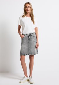 Rok denim abu-abu dengan potongan lurus, kantong samping, dan pinggang dengan loop sabuk. Dipadukan dengan atasan lengan pendek putih dan sepatu sneaker putih.
