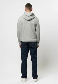 Grijze hoodie met een grote, zachte capuchon en lange mouwen, gecombineerd met donkerblauwe jeans met contrasterende stiksels en achterzakken, gedragen met witte schoenen.