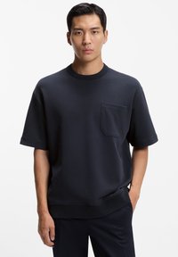 Dunkelblaues, übergroßes T-Shirt mit kurzen Ärmeln aus weicher Baumwolle, mit rundem Hals und einer Brusttasche auf der linken Seite. Glatte Textur und lockere Passform.