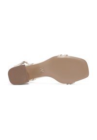Sandale à talons hauts beige avec un orteil carré et une semelle en caoutchouc texturé, dotée de brides de cheville réglables et d'accents métalliques.