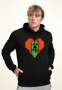Felpa nera con cappuccio caratterizzata da un personaggio pixelato verde all'interno di un grafico a forma di cuore in tonalità di arancione e rosso. Progettata con cappuccio regolabile e tasche laterali.