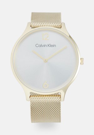Kultainen Calvin Klein -kello, jossa hopeanvärinen näyttö, minimalistinen muotoilu, verkkohihna ja kultaiset tuntimerkit klo 12 ja 6 kohdalla.