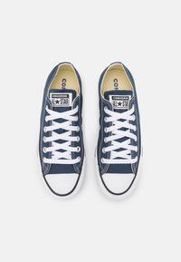 Námorní modré plátěné tenisky s bílými tkaničkami, gumovou podrážkou a černým lemem. Na jazyku se nachází logo s nápisem "Converse All Star".