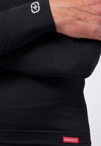Schwarzes Thermo-langärmliges Shirt mit strukturiertem Muster an den Ärmeln, enganliegendem Design und rotem "THERMOLACTYL x3"-Label am Saum.