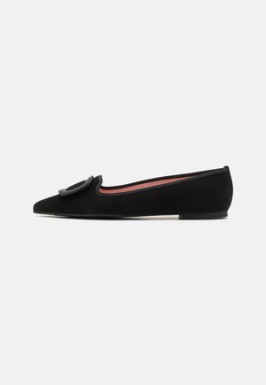 Chaussure plate en daim noir avec bout pointu et grande boucle circulaire sur le dessus, dotée d’un petit talon et d’une doublure intérieure rose.