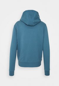 Bluza z kapturem w kolorze turkusowym, o miękkiej fakturze, z prążkowanymi mankietami i skróconym fasonem. Widok z tyłu pokazuje szczegóły szwów.