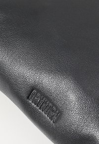 Pelle nera texturizzata con logo "DRYKORN" in rilievo. La superficie appare liscia con una leggera lucentezza e un sottile motivo grain.