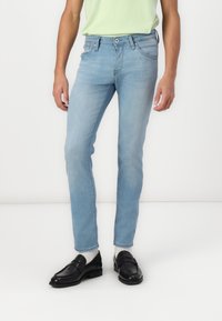 Vaqueros de mezclilla azul claro con un corte slim, diseño de cinco bolsillos y costuras en contraste. Combinados con mocasines negros y calcetines gris claro.