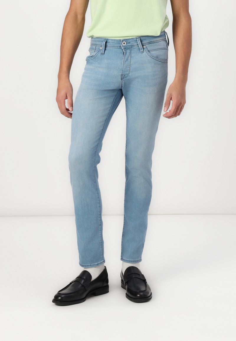 Vaqueros de mezclilla azul claro con un corte slim, diseño de cinco bolsillos y costuras en contraste. Combinados con mocasines negros y calcetines gris claro.