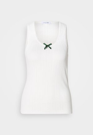 Witte mouwloze tanktop met ribbelstructuur, een V-hals en een groene strikaccent aan de voorkant. Heeft subtiele branding door het hele ontwerp.