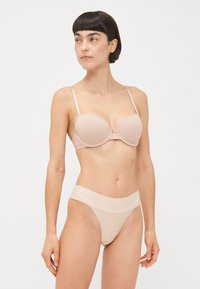 Beige polstret bh med tynne stropper, glatt stoff og en sløyfedetalj i midten. Matchende høyt midje bikini med sømløs midjebånd.