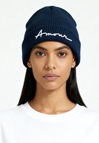 Bonnet en tricot bleu marine avec texture côtelée et revers plié présentant le mot brodé "Amour" en blanc. Design simple et décontracté.