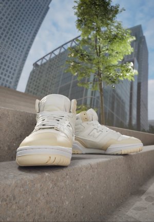 Zapatillas de caña alta en un color crema, con parte superior de cuero, detalles texturizados y un logo prominente. Presentan una suela blanca gruesa y diseño con cordones.