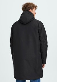 Črn plašč s kapuco in dolgim krojem, z gladko teksturo in minimalističnim dizajnom. Brez vidnih kovinskih delov ali vzorcev.