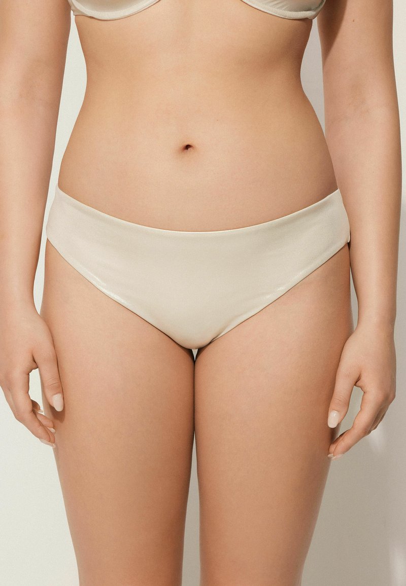 Krémové bikiny s hladkého, pružného materiálu. Mají středně vysoký pas a čisté výstřihy nohavic pro přiléhavý vzhled.