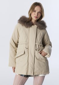 Beige gewatteerde parka met een nepbont capuchon, een cinched taille en twee voorzakken. Heeft een gladde textuur en een losse pasvorm.