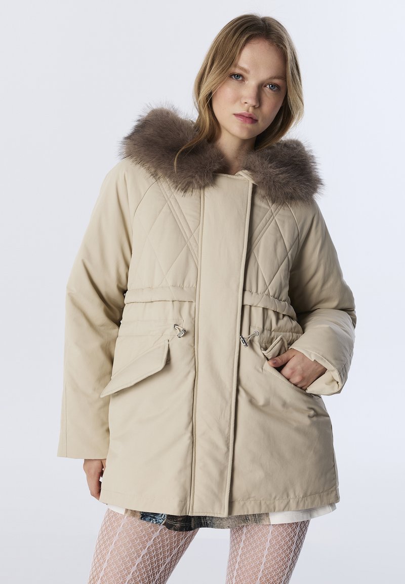 Beige gewatteerde parka met een nepbont capuchon, een cinched taille en twee voorzakken. Heeft een gladde textuur en een losse pasvorm.