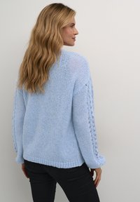 Light blue knitted sweater with a loose fit, featuring openwork detailing on sleeves and ribbed cuffs and hem. Soft, textured material.