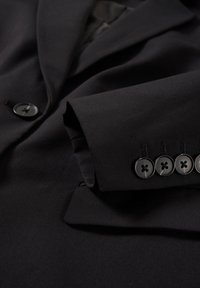 Veste de costume noire avec un revers montrant les détails des manches, comprenant cinq boutons noirs cousus près du poignet et un bouton sur le devant.