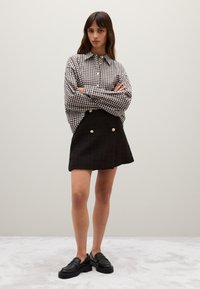 Zwart-wit geblokte blouse met lange mouwen, gecombineerd met een zwarte rok met gouden knopen en zwarte loafers als schoeisel.