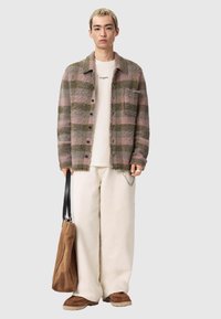 Stickad ullkofta med rosa och gröna ränder, kombinerad med en vit t-shirt, cremegula vida byxor och en brun mocka-handväska.