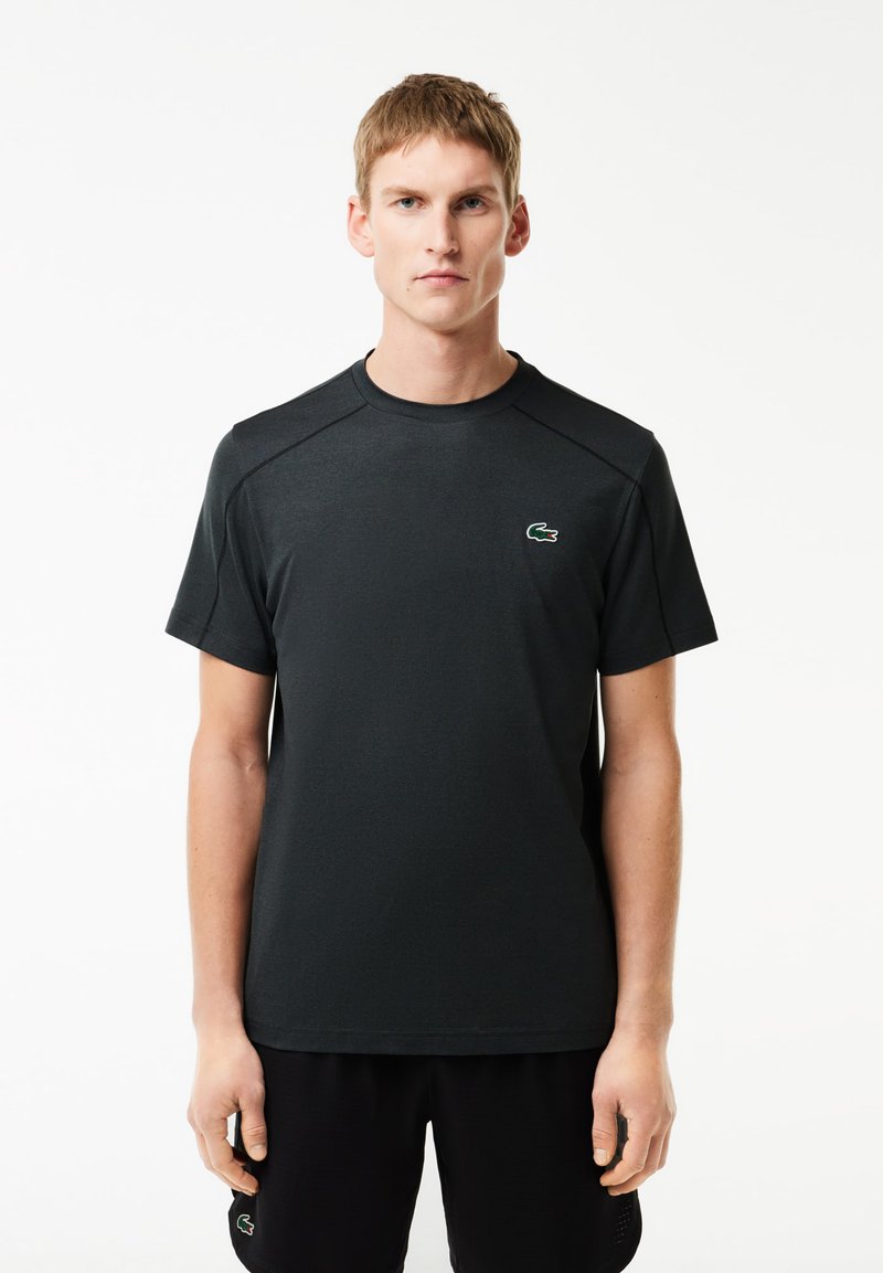 T-shirt sportivo nero realizzato in tessuto morbido, con maniche corte, colletto rotondo e un piccolo logo verde sul petto.