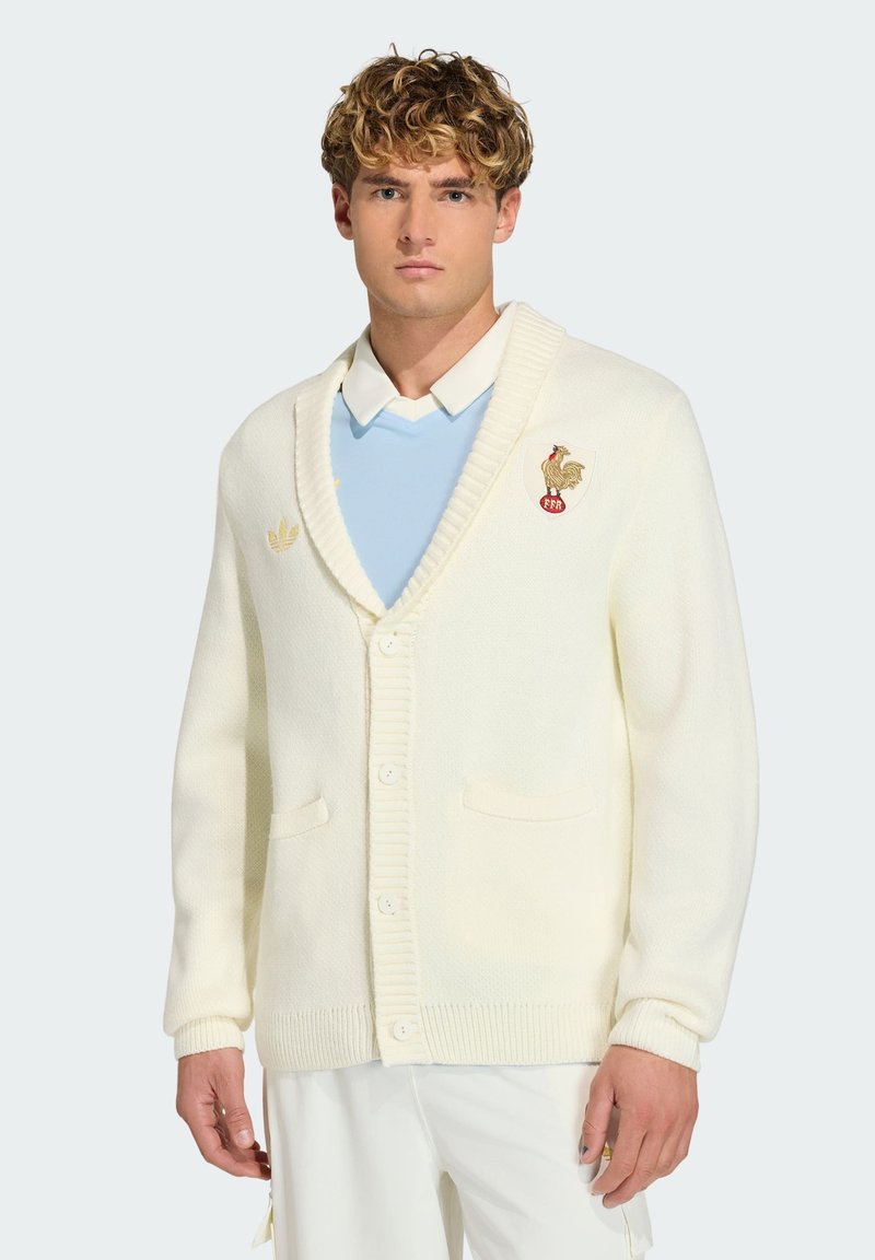 Roomkleurig vest met een textuurgebreide stof, voorzien van een sjaalkraag, geribde manchetten, een knoopsluiting en een geborduurd logo op de borst.