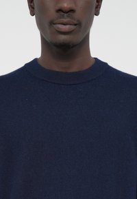Navy blue crew-neck sweater made of soft fabric; features ribbed neckline and is shown against a plain white background.