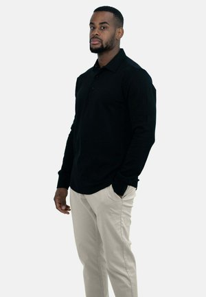 Zwarte polo met lange mouwen en een kraag, voorzien van twee knopen en een relaxte pasvorm, gecombineerd met lichtbeige broek. Gladde stof textuur.