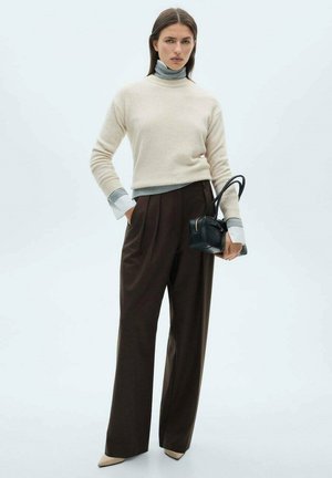 Pull en mélange de laine beige avec col roulé étroit, poignets gris, pantalon marron taille haute, et un petit sac à main noir. Talons beiges pointus.