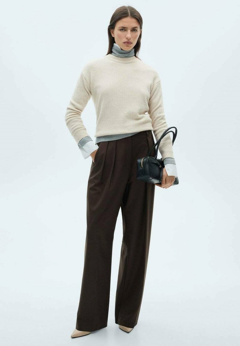 Maglione in misto lana beige con colletto alto stretto, polsini grigi, pantaloni marroni a vita alta e una piccola borsa nera. Tacchi beige a punta.