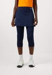 Kék sportfelső szoknya, melyhez illő capri leggings tartozik, rugalmas anyagból készült. Jellemzője a derékpánt és egy kis logó részlet.